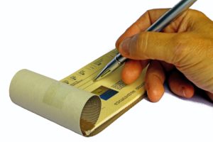 A hand writing a check with a pen.