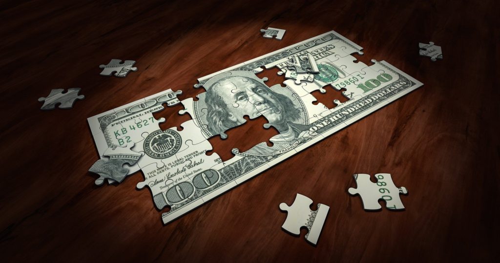 A puzzle shaped like a dollar bill with pieces missing.