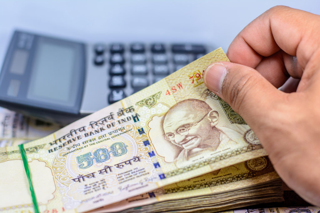calculator and a hand holding a stack of Indian Rupee money