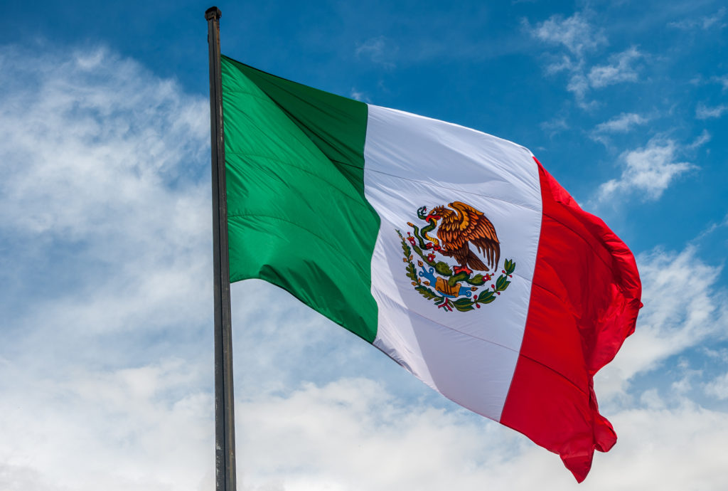 Mexican flag waving in the wind with a blue sky background